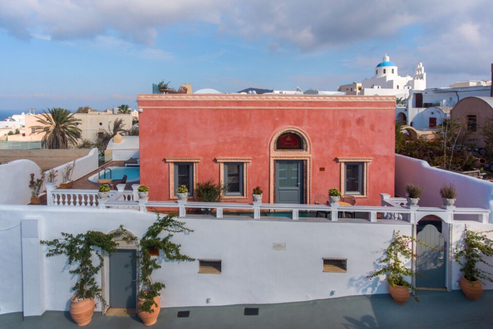 Aerial view of the dusky pink exterior of Tramonto Secret Villas, a fabulous Oia Santorini hotel with sea view